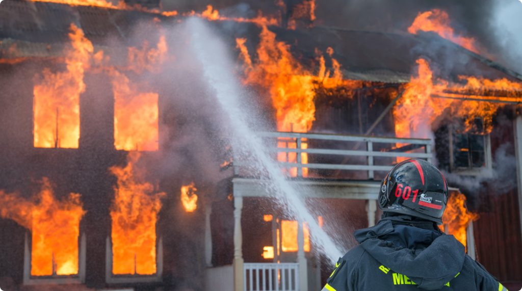 Firefighter spraying a hose on a burning home